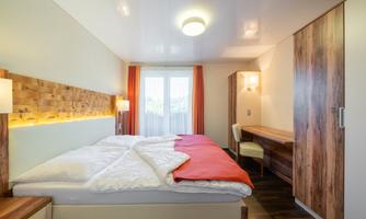 A modern bedroom with two beds and wooden details. Bright colors and a cozy atmosphere create an inviting space.
