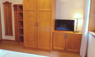 A cozy bedroom with wooden wardrobes and a television. An elegant mirror and a window provide additional light.