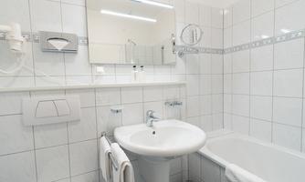 A modern bathroom with white tiles and a bathtub. There is a sink, a mirror, and toiletries.