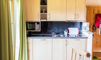 A bright, modern kitchen with wooden cabinets and a black countertop. It is equipped with a microwave, sink, and kitchen utensils.