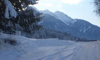 A snowy landscape with mountains in the background. The path is surrounded by snow and trees.