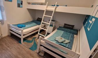 A bright bedroom with two single beds and a bunk bed. The bedding is in shades of blue, and the room has a cozy atmosphere.