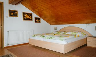 A cozy bedroom with a large bed and wooden ceilings. Some pictures hang on the wall, and the room has a warm, inviting character.