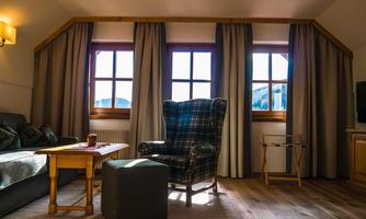 A cozy living room with a large armchair and a small table. Outside, the sun is shining through the windows.