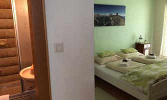 A cozy bedroom with a large bed and fresh colors. In the background, there is a modern bathroom with a shower.