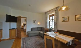 A cozy living area with a sofa, a dining table, and a television. Bright walls and a window create a friendly atmosphere.