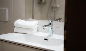 A modern bathroom with a white sink and a faucet. Freshly stacked towels are resting on the sink.