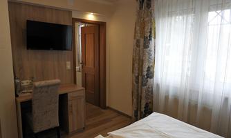 A modern hotel room with a television on the wall and a desk. Bright curtains let in plenty of light.