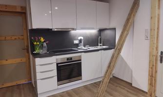 A modern kitchen with white cabinets and a dark countertop. On the wall stands a vase with fresh flowers.