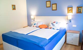 A cozy bedroom with a white bed and blue bed linens. There are some pictures hanging on the walls, and there is soft lighting.