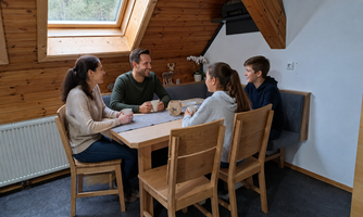 A family of four is sitting at a table in a cozy room with wooden paneling. They appear relaxed and are having a cheerful conversation.