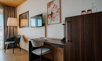 A modern hotel room with a desk, a TV, and a refrigerator. Soft colors and floral décor create a cozy atmosphere.