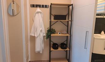 An elegant entrance area with a towel holder and an open shelf. The shelf contains decorative elements and baskets, and a bathrobe hangs ready to wear.