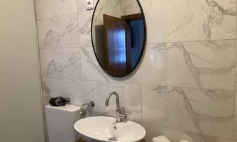 A modern bathroom with a round mirror above a white sink. The walls are clad with bright, marbled tiles.