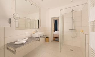 A modern bathroom with bright tiles and a large shower. The wash area is elegantly equipped with a large mirror and towels.