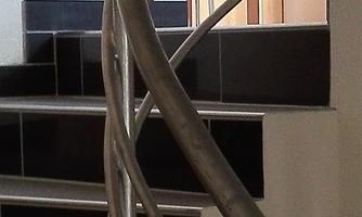 A curved staircase with a metal railing. In the background, there is a room with a table and a chair visible.