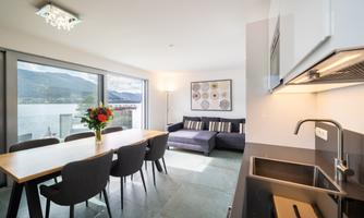 A modern living room with a large dining table and a cozy couch. Large windows offer a view of the landscape and plenty of daylight.