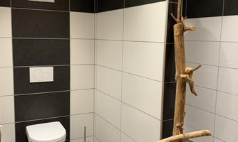 A modern bathroom with black and white tiles. On the left side is a toilet and a decorative wooden stela.