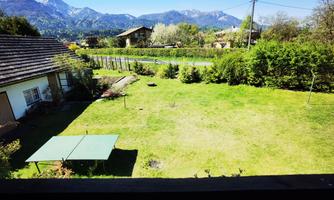 A spacious garden with lawns and a table tennis table. In the background, green bushes and mountains can be seen.