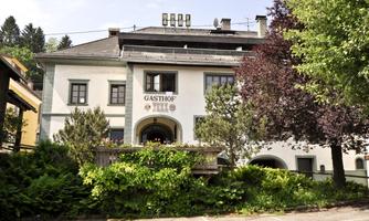 A traditional inn with a green environment. The facade is bright and inviting, surrounded by trees.