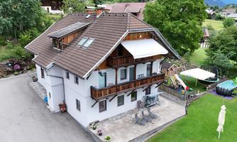 A charming house with a large balcony and a well-maintained garden. In the background, trees and a tranquil environment are visible.