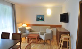 A cozy living room with a sofa, a table, and a television. There are large windows that let in a lot of daylight.