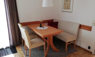 A bright dining room with a wooden table and comfortable chairs. Curtains and a decorative picture give the room a cozy atmosphere.