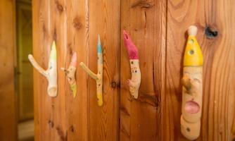 A wooden board with several colorful, handcrafted figures representing faces and hands. The figures are painted differently and attached to the wall.