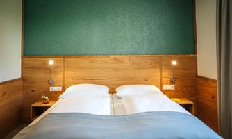 A cozy bedroom with a double bed and modern wood interior. The wall is painted in a calming green.