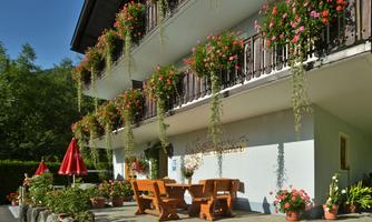 A beautiful building with a balcony decorated with flowers. Below are wooden chairs and tables as well as some umbrellas.