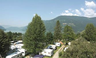 A campsite with many RVs near a lake. In the background, there are green hills and a blue sky.