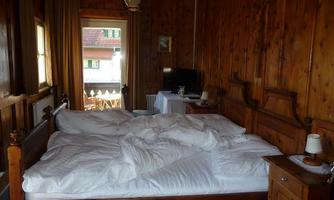 A cozy room with wooden walls and a large bed. The room has a window with an outward view and simple furniture.