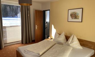 A cozy bedroom with a double bed and two large pillows. The room has a balcony that offers a view of the winter landscape.