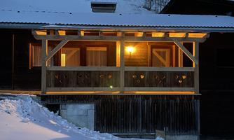 A cozy wooden house in the snow with a illuminated porch. The atmosphere is warm and inviting in the cold surroundings.