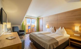 A modern hotel room with wood paneling, two beds, and a small balcony. Cozy furniture and bright lighting create a relaxed atmosphere.