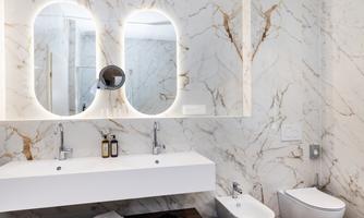 A modern bathroom with elegant marble and two round mirrors. The furnishings are simple and stylish, with a sink and a toilet.