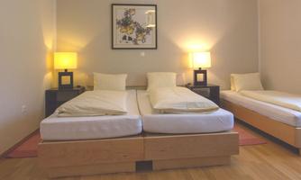 A bright bedroom with two single beds and an additional bed. Two nightstands with lamps and a picture on the wall create a cozy atmosphere.