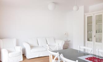 A bright and cheerful living room with white sofas and a table. The room has a modern, minimalist style.
