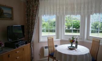 A cozy dining area with a round table and chairs. Large windows provide a view of the green landscape outside.