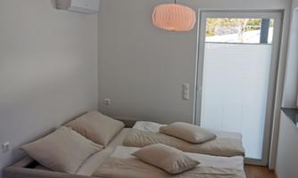 A modern room with two beds and large windows. There is a small table and a minimalist decor.