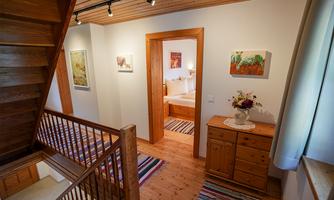 A bright staircase with wooden details and a colorful carpet. In the background, a bedroom is visible, decorated with artworks and fresh flowers.