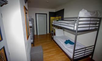 A simple room with a bunk bed and a small seating area. The floor is wooden and the walls are painted light.
