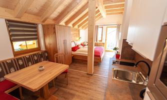 A cozy wooden apartment with an open living area. It has a kitchen, a dining area, and a bedroom with access to the balcony.