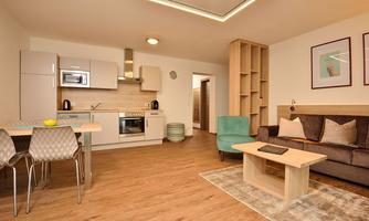 A modern living room with an open kitchen. There is a dining table, a comfortable armchair, and a couch in the room.