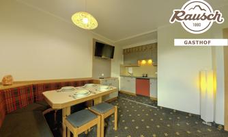 A cozy dining area with a long table group and upholstered chairs. The modern kitchen is well equipped, and in the background, there is a television.
