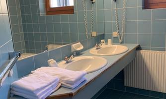 A bathroom with blue tiles and a large sink. Fresh towels are ready on the shelf.