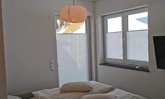 A modern bedroom with a large bed and two pillows. The room has light walls and large windows that let in light.