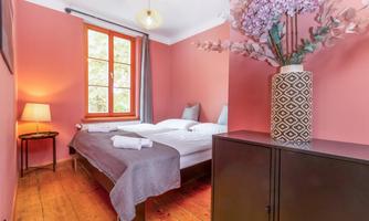 A cozy bedroom with two beds and a warm, pink wall color. A modern lamp and a decorative flower pot give the room an inviting atmosphere.