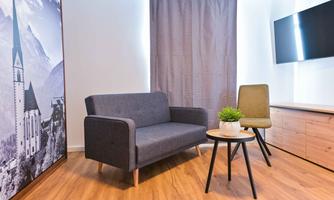 A modern living room with a gray sofa, a green chair, and a small table. On the wall is a large, monochrome picture and the room has a bright, inviting atmosphere.
