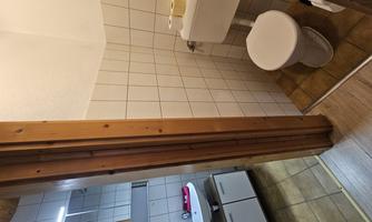 A small bathroom with a toilet and a sink. The walls are tiled and there are wood accents.